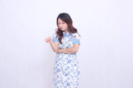Photo for Beautiful Javanese Chinese girl pouting wearing a modern Chinese dress with her arms crossed pointing to the bottom left on a white background. happy Chinese New Year - Royalty Free Image