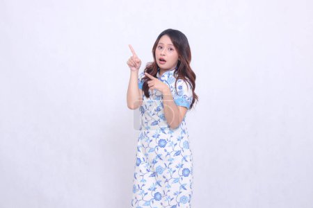 Beautiful shocked Javanese Chinese woman wearing a modern Chinese dress, front view, all hands pointing to the upper right side on a white background. happy Chinese New Year