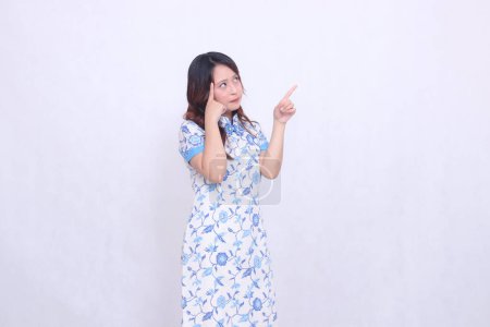 beautiful Javanese Chinese woman thinking wearing a modern Chinese dress showing her brain and hand pointing up left on a white background. happy Chinese New Year