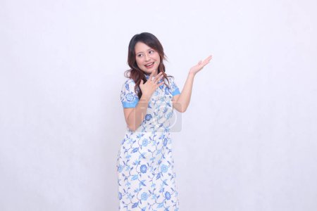 Photo for Beautiful cheerful Javanese Chinese girl wearing modern Chinese dress looking left and hand presenting isolated white background. happy Chinese New Year - Royalty Free Image