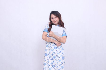 Photo for Beautiful Chinese Indonesian woman smiling wearing modern Chinese blue dress hugging tablet and pen isolated white background - Royalty Free Image