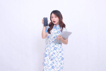 Photo for Beautiful Asian woman wearing blue Chinese dress holding tablet and looking at cellphone screen isolated on white background - Royalty Free Image