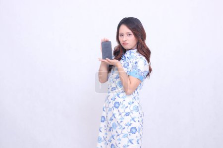 Photo for Young asian javanese chinese girl wearing blue traditional chinese dress cheongsam shocked happy promoting and holding gadget on cell phone screen isolated white background - Royalty Free Image