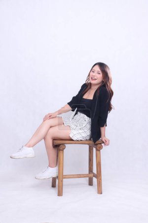 cuerpo completo hermosa chica asiática 20s formal oficina elegante sexy sonrisa alegre sentado en silla de madera aislado fondo blanco