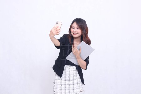 Foto de Hermosa sudeste asiático mujer 20s formal oficina riendo mirando celular y llevando tableta para promo aislado blanco fondo - Imagen libre de derechos