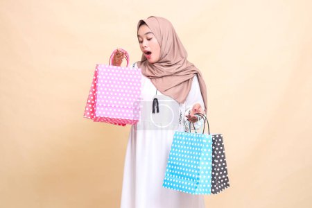 El encanto de una joven musulmana asiática que llevaba un hiyab se sorprendió al ver lo que había dentro, llevando una colorida bolsa de papel con variaciones hacia arriba y hacia abajo. para publicidad, estilo de vida, banners y Ramadán