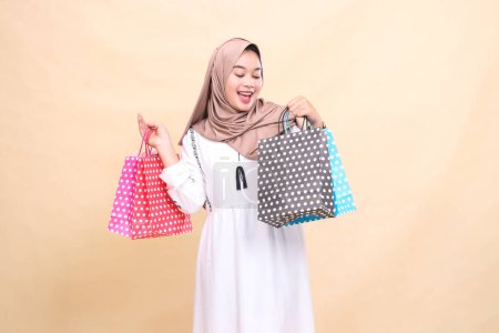 Photo for The charm of a young indonesia Muslim woman wearing a hijab is candid and cheerful, looking and carrying colorful paperbags with variations up and down. for advertising, lifestyle, banners and Ramadan - Royalty Free Image