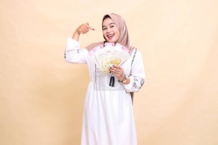 portrait of a beautiful Asian Muslim woman wearing a hijab, smiling cheerfully, receiving a gift or fitrah on Eid. used for advertising, giveaways, Eid and Ramadan