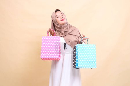 el encanto de una joven musulmana asiática que lleva un hiyab con una sonrisa elegante que lleva un colorido bolso de papel de compras de arriba hacia abajo. para publicidad, estilo de vida, banners y Ramadán