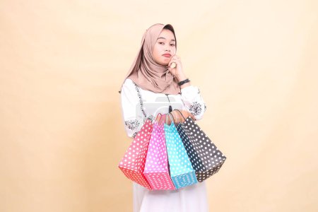 la historia de una joven musulmana asiática en un hiyab haciendo pucheros, sosteniendo su mejilla y llevando una bolsa de compras. para publicidad, cultura, Eid y Ramadán