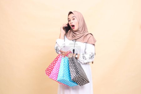 a young indonesia Muslim woman wearing a hijab was shocked by someone's phone call and carrying a paper bag. for advertising, technology, Eid and Ramadan