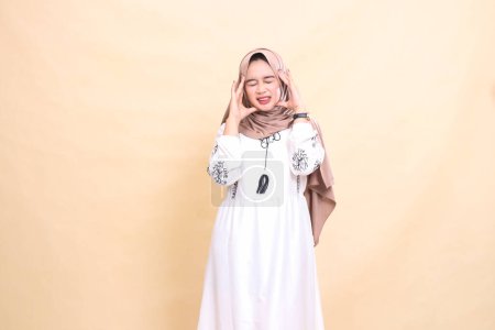 Aufrichtiges Porträt einer erwachsenen indonesischen Muslimin im Hijab, die ihren Kopf hält und starke Kopfschmerzen hat. für Werbung, Gesundheit, Wissenschaft und Ramadan