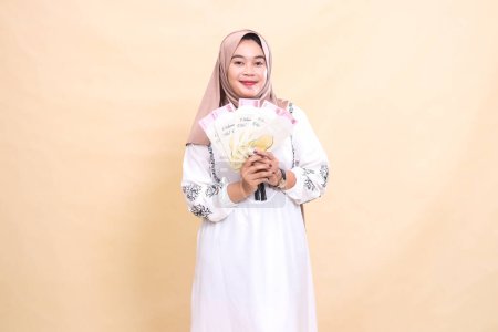 Porträt einer schönen asiatischen Muslimin im Hijab mit einem anmutigen Lächeln, die ein Geschenk oder eine Fitra an Eid hält. verwendet für Werbung, Werbegeschenke, Eid und Ramadan