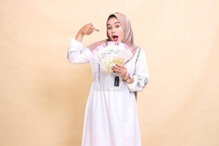 Portrait of a beautiful Asian Muslim woman wearing a hijab, surprised to show gifts and gifts on Eid. used for advertising, giveaways, Eid and Ramadan