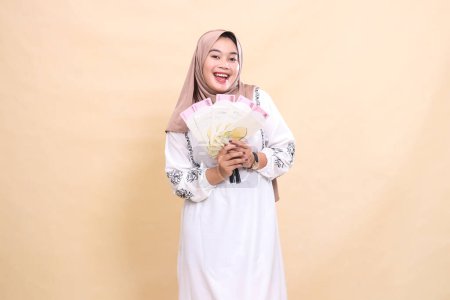 Porträt einer schönen indonesischen Muslimin, die einen Hijab trägt und glücklich lächelt, während sie ein Geschenk oder eine Fitrah an Eid hält. verwendet für Werbung, Werbegeschenke, Eid und Ramadan