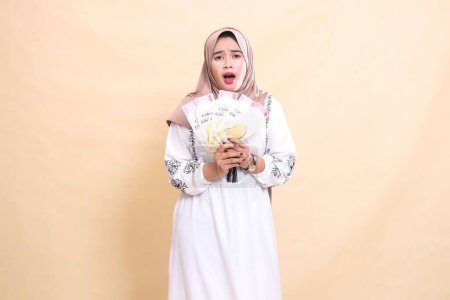 Foto de Retrato de una hermosa mujer musulmana asiática con un hiyab, conmocionada y triste, sosteniendo un regalo o fitrah en Eid. utilizado para la publicidad, regalos, Eid y Ramadán - Imagen libre de derechos
