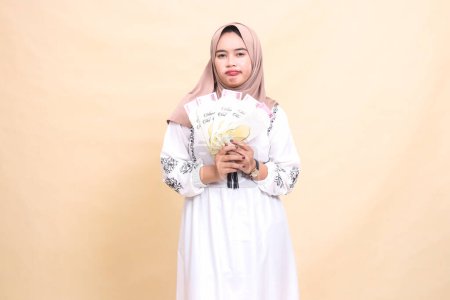 Foto de Retrato de una hermosa mujer musulmana indonesia usando un hiyab, hosco y decepcionado, sosteniendo un regalo o fitrah en Eid. utilizado para la publicidad, regalos, Eid y Ramadán - Imagen libre de derechos
