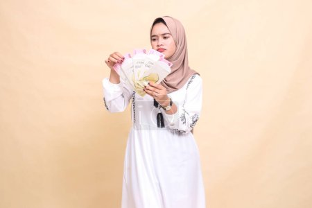 Porträt einer schönen indonesischen Muslimin, die einen Hijab trägt und Geschenke und Geschenke am Eid mürrisch hält und zählt. verwendet für Werbung, Werbegeschenke, Eid und Ramadan