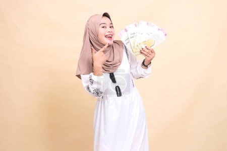 Portrait of a beautiful Asian Muslim woman wearing a cheerful hijab holding and showing gifts and gifts to the left on Eid day. used for advertising, giveaways, Eid and Ramadan