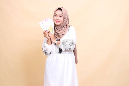 portrait of a beautiful Asian Muslim girl wearing a hijab smiling gracefully, holding and showing off gifts and gifts to the right on Eid day. used for advertising, giveaways, Eid and Ramadan