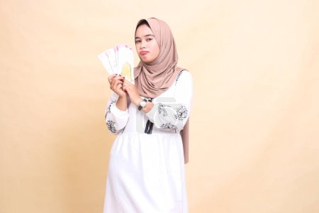 Portrait of a beautiful Asian Muslim woman wearing a hijab, sullenly holding and showing off gifts and gifts to the right on Eid day. used for advertising, giveaways, Eid and Ramadan