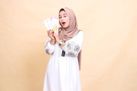 Portrait of a beautiful indonesia Muslim woman wearing a hijab looks up holding and showing off a gift or fitrah to the right on Eid day. used for advertising, giveaways, Eid and Ramadan
