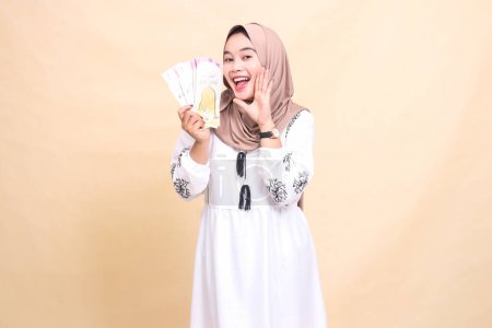 portrait of a beautiful Asian Muslim woman wearing a hijab, smiling cheerfully, showing off gifts and gifts while showing off gifts to the right on Eid. used for advertising, giveaways and Ramadan