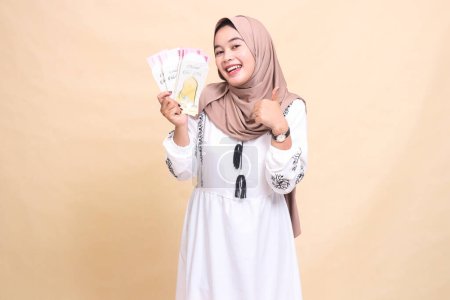 portrait of a beautiful Asian Muslim girl wearing a hijab smiling wearing a hijab holding and showing off gifts and gifts to the right on Eid. used for advertising, giveaways, Eid and Ramadan