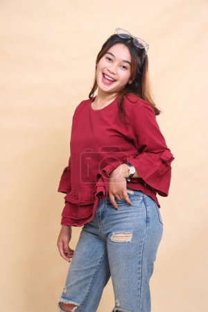 Belle femme élégante indonesia en chemise rouge, heureuse, les mains dans les poches et droit vers le bas en regardant la caméra. utilisé pour la mode, la publicité et le contenu industriel