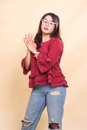 Beautiful elegant Asian woman in red shirt, cool expression, hands holding each other, wearing glasses. used for fashion, advertising and industrial content