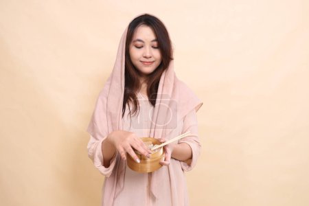 Foto de Mujer asiática con una sonrisa de hiyab sosteniendo un cuenco de madera frente a ella que contiene delicioso y delicioso dimsum - Imagen libre de derechos