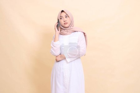 Photo for Asian Muslim woman wearing a candid hijab holding a cellphone gadget in her hand while calling someone. Lifestyle, technology and promotion concept - Royalty Free Image