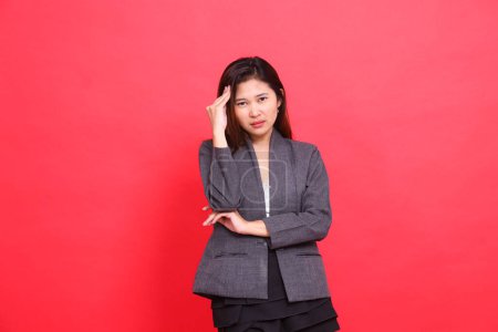 The expression of an Asian office woman with her arms crossed, having a headache while holding the camera, wearing a gray jacket and red skirt. for health, business and advertising concepts