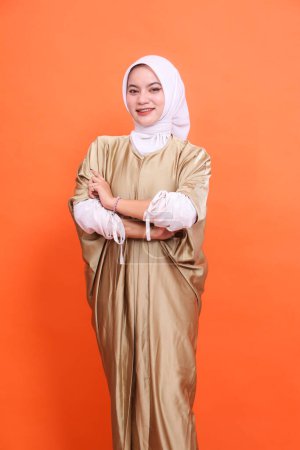 Young asian Muslim woman in hijab isolated orange background. standing with a smile with his arms crossed, wearing a Muslim kaftan. Half body portrait for religious, fashion, educational concepts