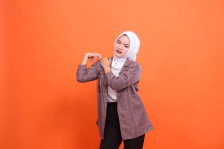 Portrait of beautiful young asian sick woman in hijab candid, Experiencing shoulder pain fatigue, putting hand on shoulder with orange studio background. Lifestyle, health care, commercial concept