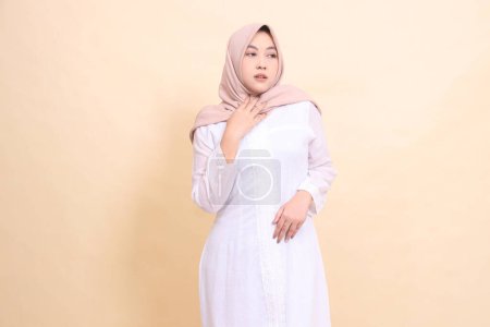 Frau Indonesien schön trägt ein weißes Kleid und braunen Hijab steht offen mit ihren Händen hält ihren Hals (nassen Husky). für Gesundheits-, Pflege-, Bildungs- und Wissenschaftskonzepte