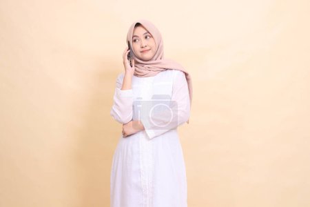 Photo for Girl asian muslim wearing a hijab candid smile holding a cellphone gadget in her hand while calling someone. Lifestyle, technology and promotion concept - Royalty Free Image