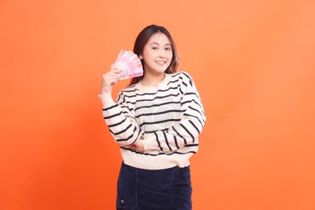 The expression of a cheerful Asian woman standing while holding a number of rupiah bills in her arms. for fashion, business and finance concept