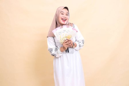 Foto de Retrato de una hermosa mujer musulmana asiática con un hiyab sonriendo felizmente sosteniendo un regalo o fitrah en Eid. utilizado para la publicidad, regalos, Eid y Ramadán - Imagen libre de derechos