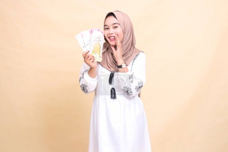 Foto de Retrato de una hermosa mujer musulmana indonesia usando un hiyab, sonriendo y sosteniendo una sonrisa mientras muestra regalos y regalos a la derecha en el Eid. utilizado para la publicidad, regalos, Eid y Ramadán - Imagen libre de derechos