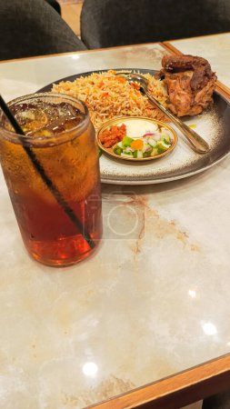 portrait of kebuli rice (nasi kebuli) and iced tea, typical Arabic food made in Indonesia on a table with empty space beside it at a 45 degree angle