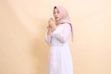 Mädchen Indonesien trägt einen Hijab, weißes Kleid, steht offen, bedeckt ihre Augen, Mund leicht geöffnet, niest. für Gesundheit, Pflege, Bildung und naturwissenschaftliche Inhalte