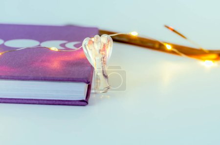 Foto de Cerca de cristal de ángel de cuarzo claro cerca de un diario de la luna con luces de Navidad e incienso en el fondo. Concepto: prácticas espirituales de autocuidado - Imagen libre de derechos