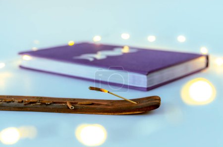 Foto de Cierre la varilla de incienso ardiendo con un diario de la luna con luces de Navidad de fondo. Concepto: prácticas espirituales de autocuidado - Imagen libre de derechos
