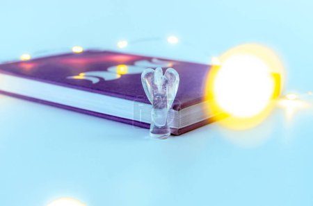 Foto de Cerca de cristal de ángel de cuarzo claro cerca de un diario de la luna con luces de Navidad e incienso en el fondo. Concepto: prácticas espirituales de autocuidado - Imagen libre de derechos