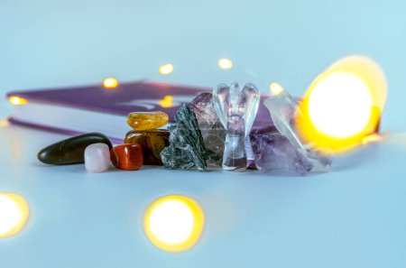 Foto de Primer plano de cristales curativos coloridos semi-preciosos con luces navideñas bokeh y diario sobre un fondo blanco - Imagen libre de derechos