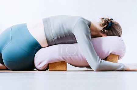 Frau macht restaurativen Yoga-Twist mit Polster auf Korkblöcken