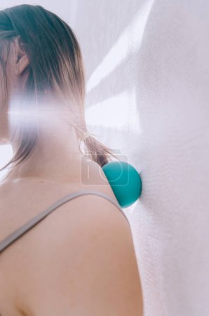 Mujer haciendo ejercicio MFR espalda con bola de masaje terapia en la pared