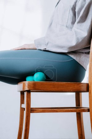 Mujer haciendo recuperación de isquiotibiales con bolas de terapia sentada en silla