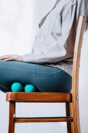 Frau macht Beinmassage zur Erholung mit Therapiebällen im Sitzen auf Stuhl